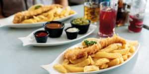 Plates of fish and chips with sauces and drinks on a table at Harbour Lights, reflecting the restaurant’s award winning seaside dining.