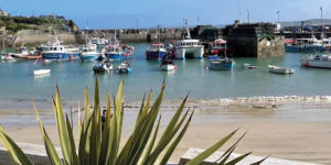 View across Newquay Harbour with fishing boats on the water and sandy shore beyond, capturing the harbourside setting near The Boathouse.