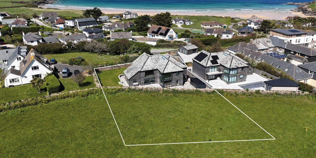 Aerial view of two modern coastal homes, with a marked plot of land and a sandy beach beyond.