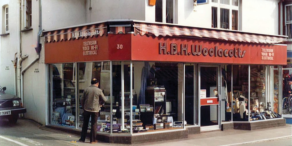 Historic exterior of the Woolacotts shopfront, with television, radio and electrical products displayed in the window.