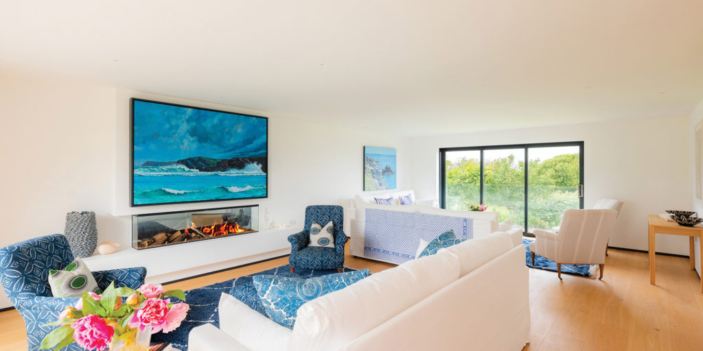 Bright living room with blue and white coastal styling, a fireplace, large artwork and sliding doors to the garden.