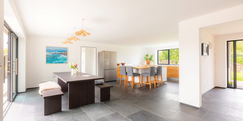 Modern open-plan kitchen and dining space with wooden cabinetry, slate flooring and large glass doors leading outside.