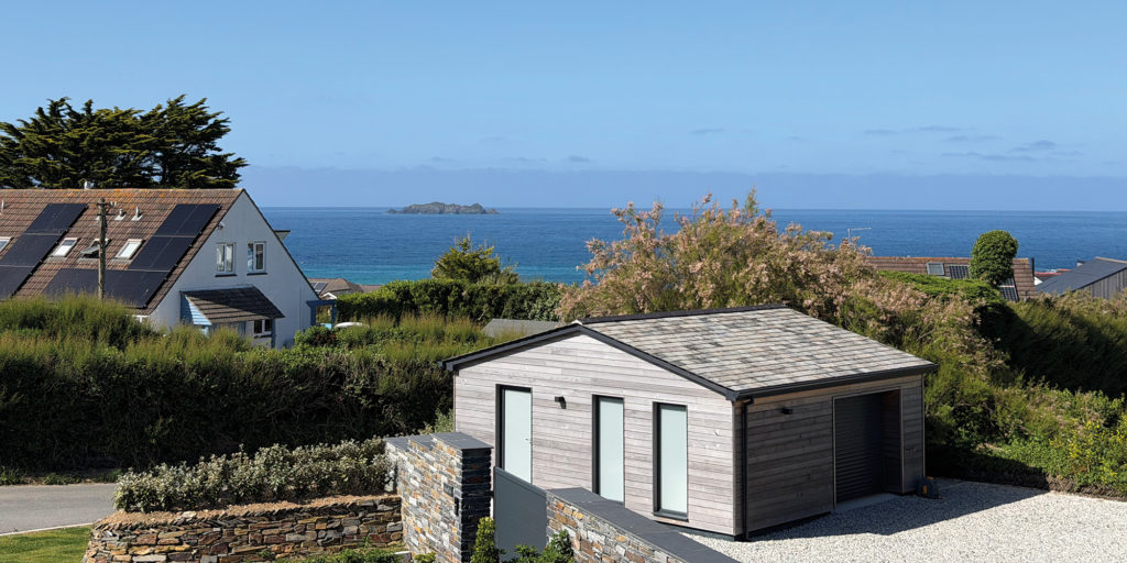 Coastal view from a property, looking across rooftops and gardens towards the sea and distant rocks.